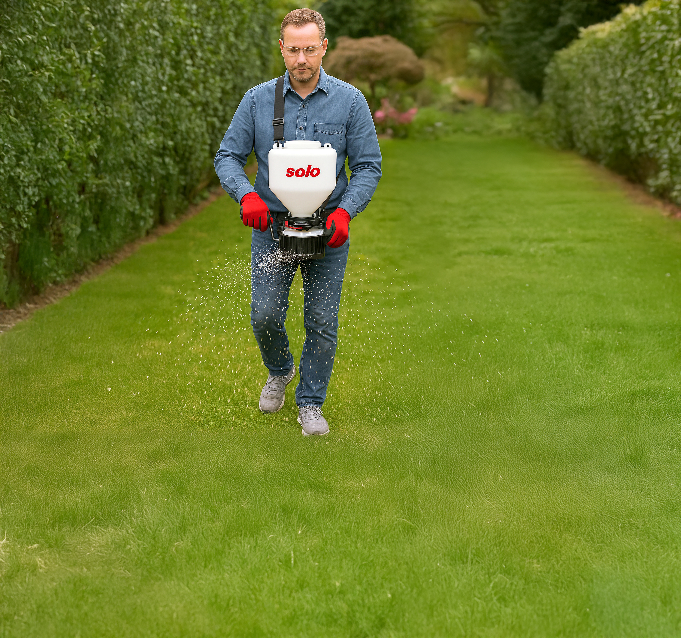 Einsatz des SOLO 421 Granulatstreuers im Garten Ein Mann streut gleichmäßig Granulat über eine grüne Rasenfläche, während er den SOLO 421 Granulatstreuer mit Schultergurt vor dem Körper trägt.