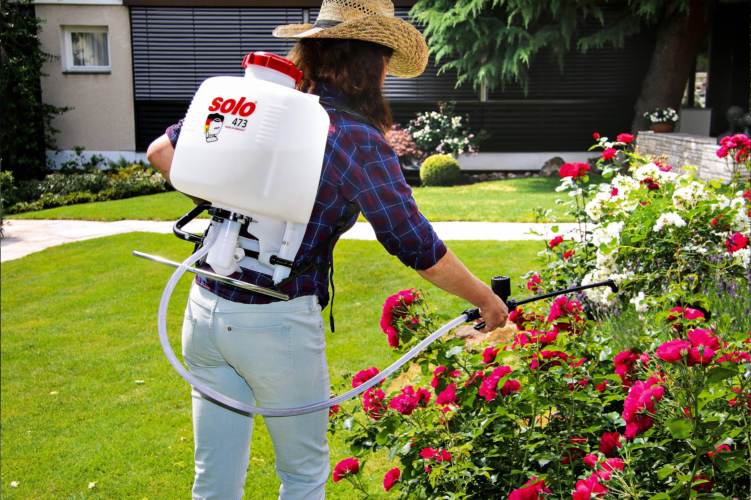 Gärtnerin mit Solo 473 Rückenspritze beim Pflanzenschutz im Garten Eine Gärtnerin mit Strohhut sprüht Rosen in einem gepflegten Garten mit einer Solo 473 Rückenspritze für Pflanzenschutzmittel.