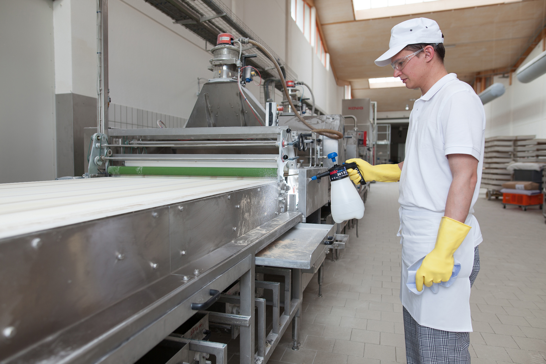 Mitarbeiter reinigt Produktionsmaschine mit SOLO 301 B Handsprüher in Lebensmittelbetrieb Mann mit gelben Handschuhen und SOLO 301 B Handsprüher reinigt eine Edelstahlmaschine in einer Lebensmittelproduktion.