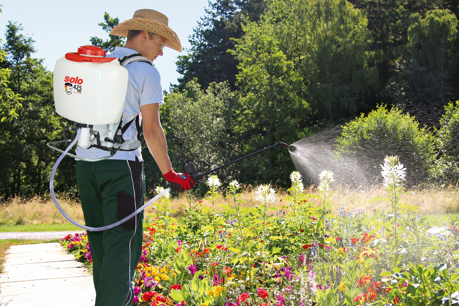 Gärtner mit SOLO 425 PRO Rückenspritze beim Pflanzenschutz im Blumenbeet Mann mit Strohhut und SOLO 425 PRO Rückenspritze besprüht ein bunt blühendes Blumenbeet bei sonnigem Wetter.